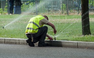 Technician adjusting a sprinkler head beside a street in Killeen